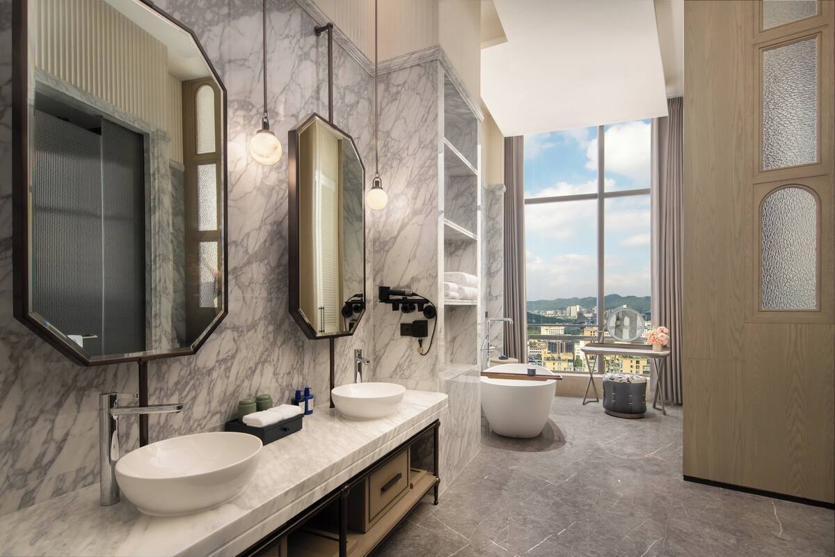 A modern bathroom with two sinks, a large mirror, and a bathtub.