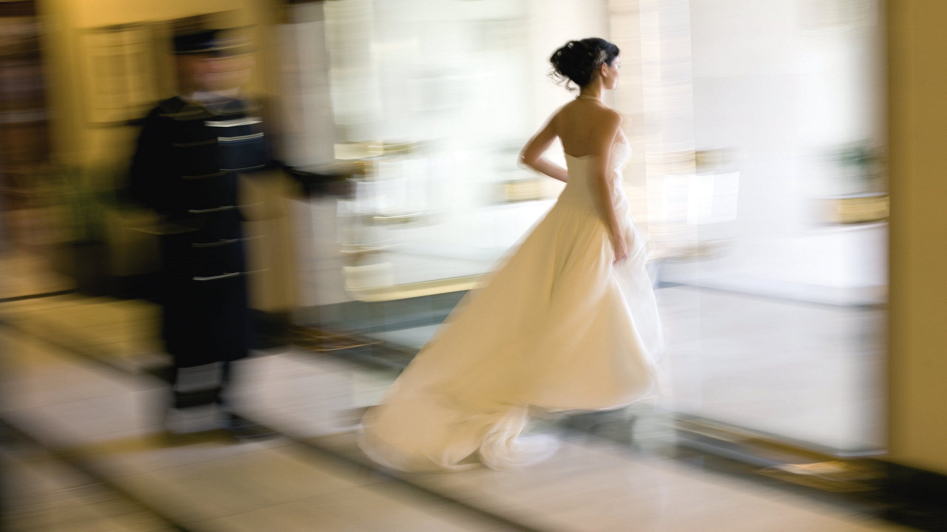 Escena borrosa de una persona con vestido blanco caminando por una puerta.