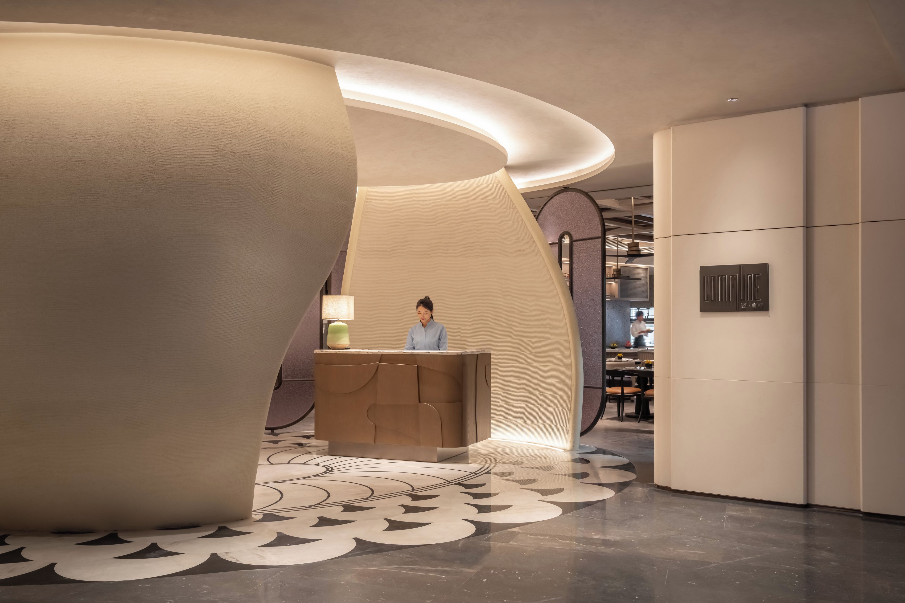 A modern hotel lobby with a reception desk, a large decorative pillar, and a patterned floor.