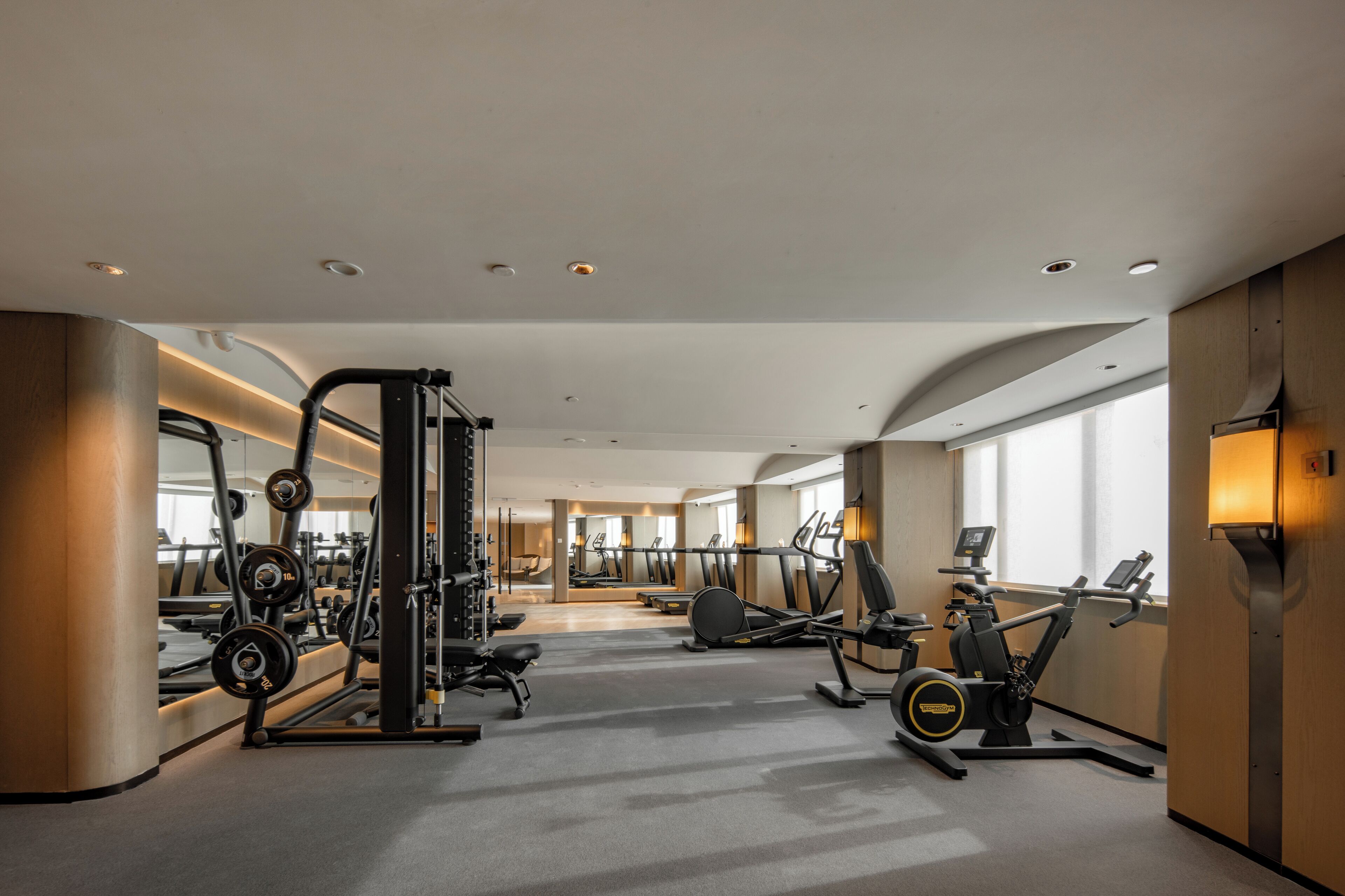 A modern hotel gym with cardio machines, weight stations, and a large mirror.