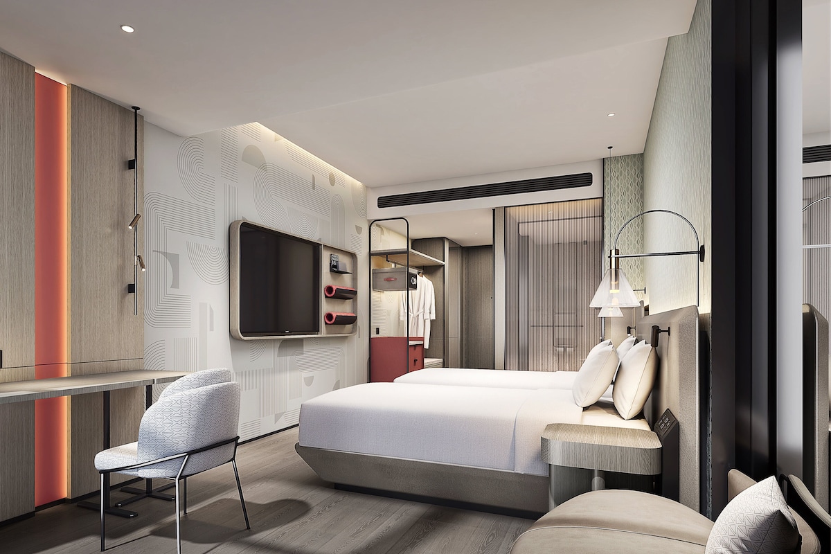 A modern hotel room with a large bed, a desk, a chair, and a TV.