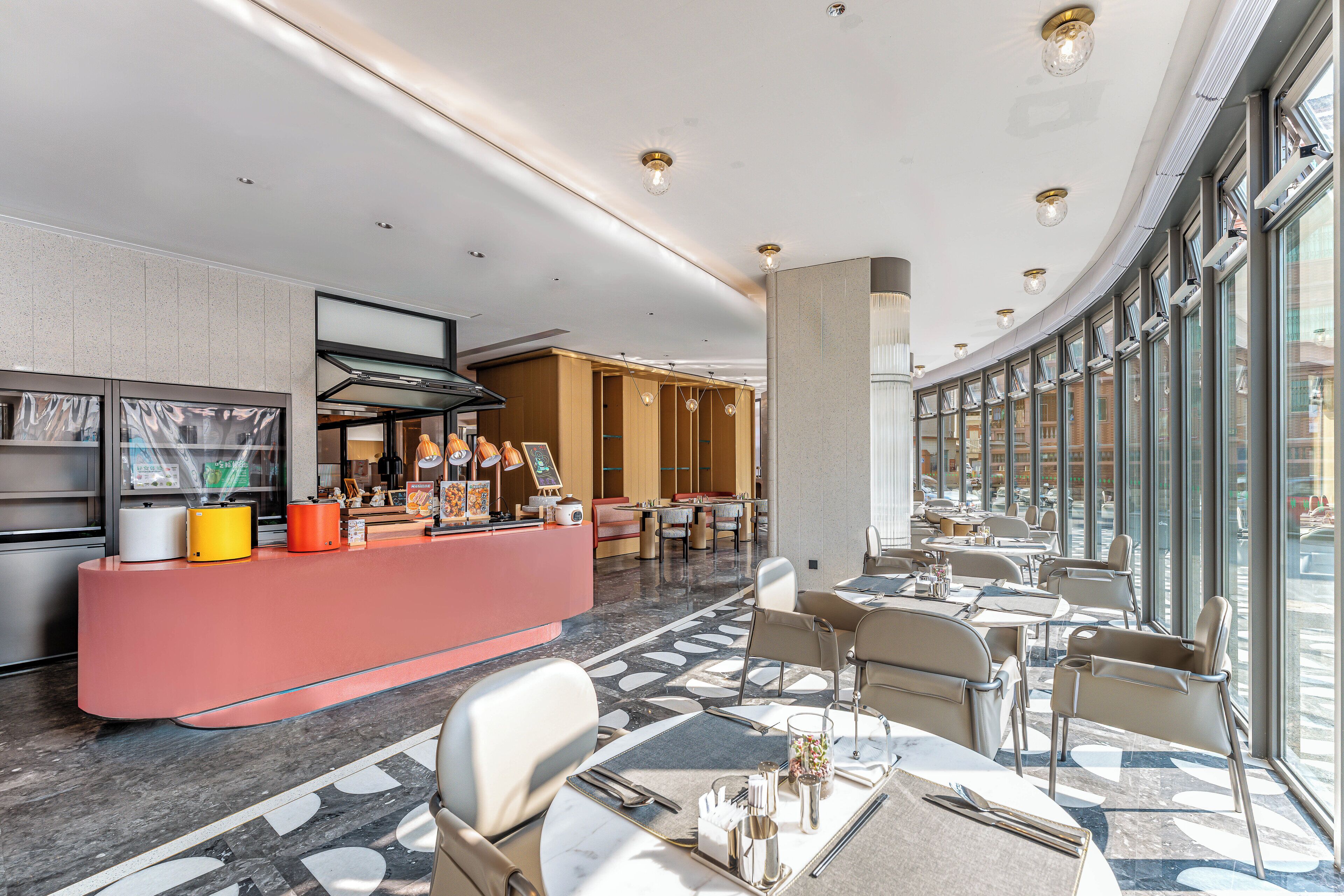 A modern hotel lobby with a central reception area, dining tables, and large windows offering views of the street.