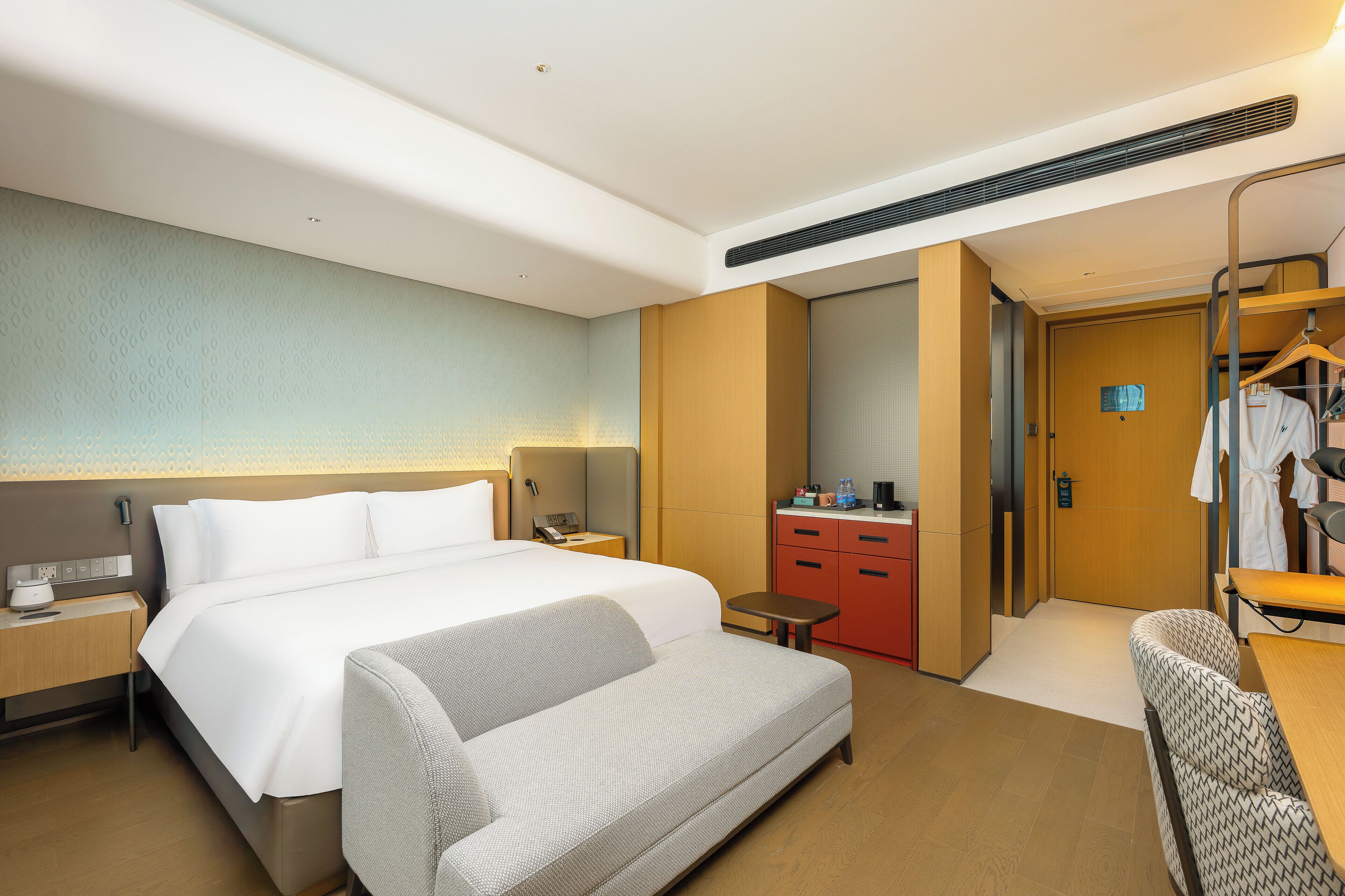 A hotel room with a large bed, a sofa, a desk, a small table, a mirror, a wardrobe, and a bathroom door.