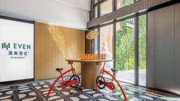 A modern hotel lobby with a large glass window, a reception desk, and a unique bicycle charging station.