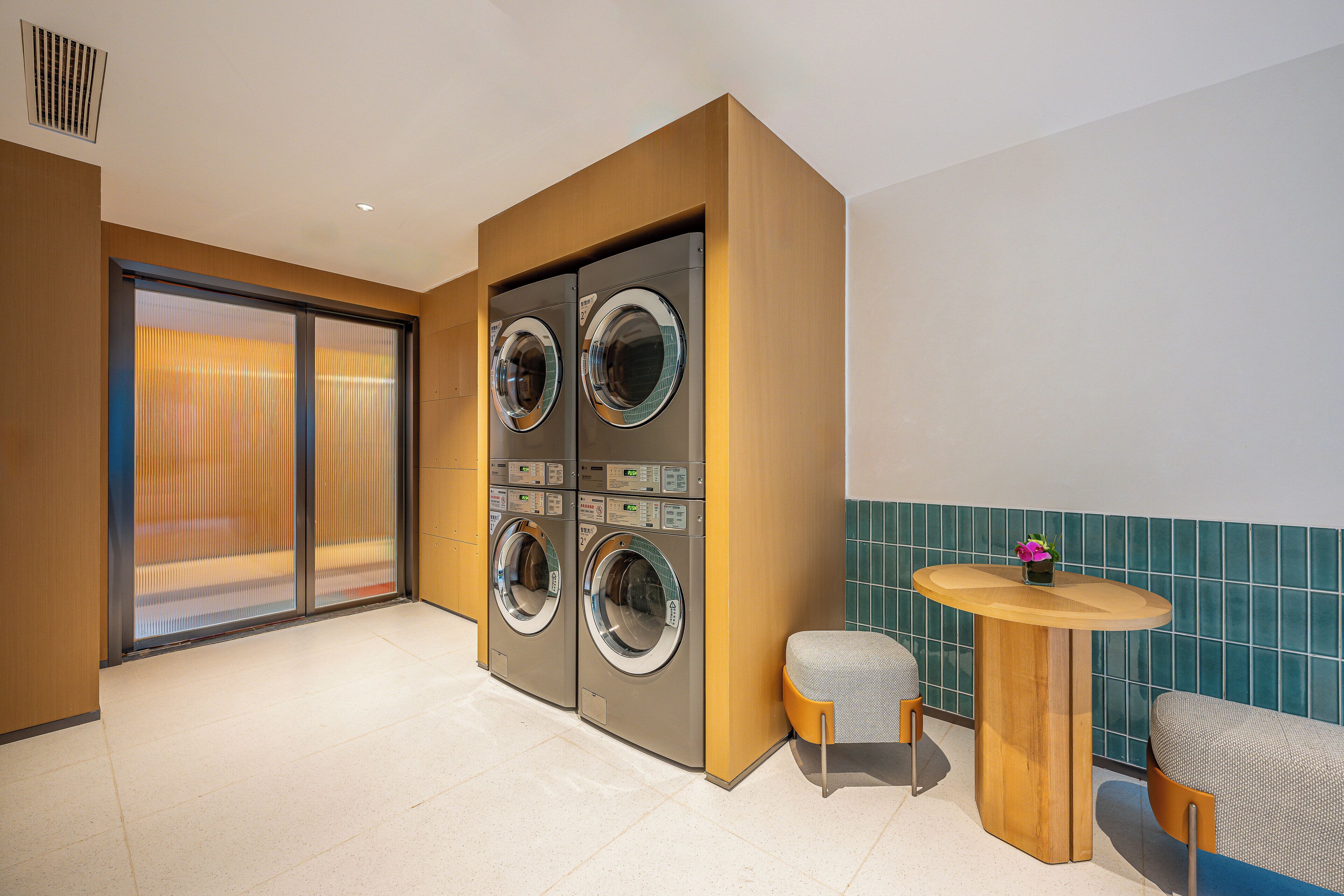 Una habitación de hotel con lavadora, una mesita y una silla.