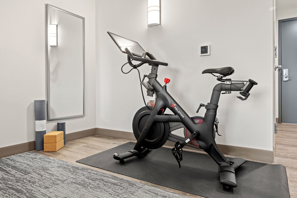 A stationary bike in a room with a mirror, a yoga mat, and a small box.
