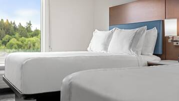 A hotel room with two beds, a wooden headboard, a bedside lamp, and a view of greenery outside.