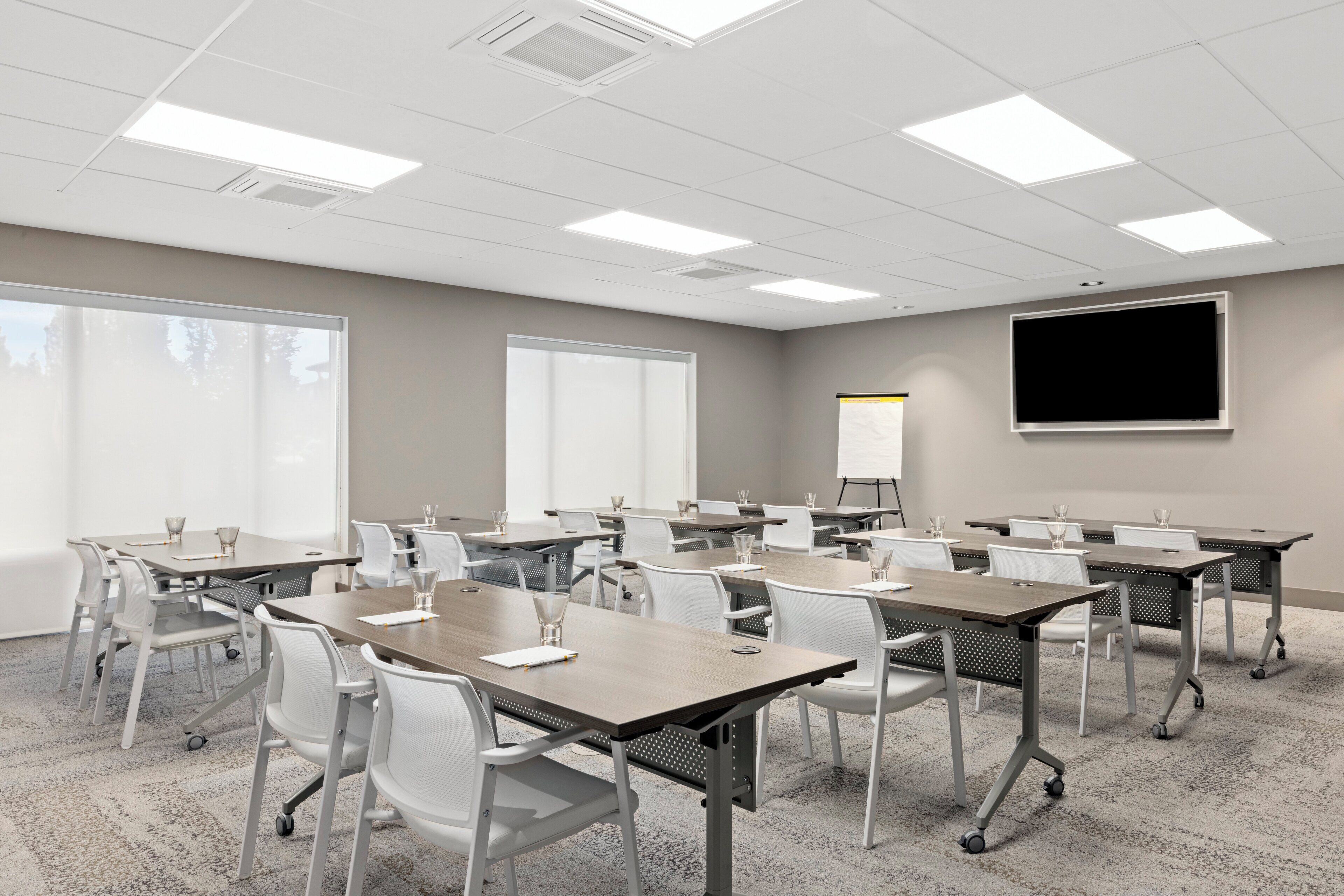 A conference room with multiple tables and chairs, a projector screen, and large windows.