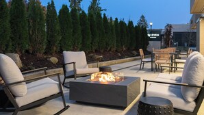 An outdoor seating area with a fire pit, lounge chairs, and a view of a building with a sign. - EVEN Hotel Portland – Beaverton by IHG (Portland)