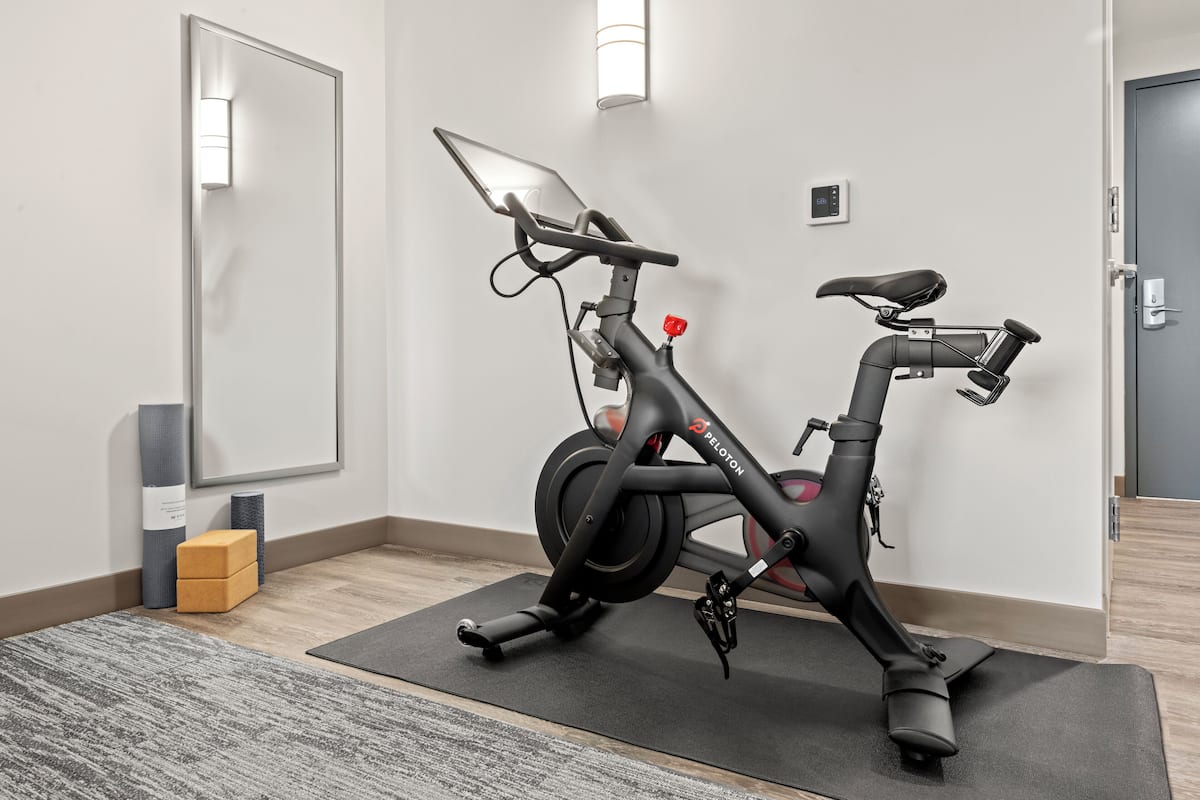 Uma bicicleta ergométrica em um quarto com um espelho, um tapete de yoga e uma pequena caixa.