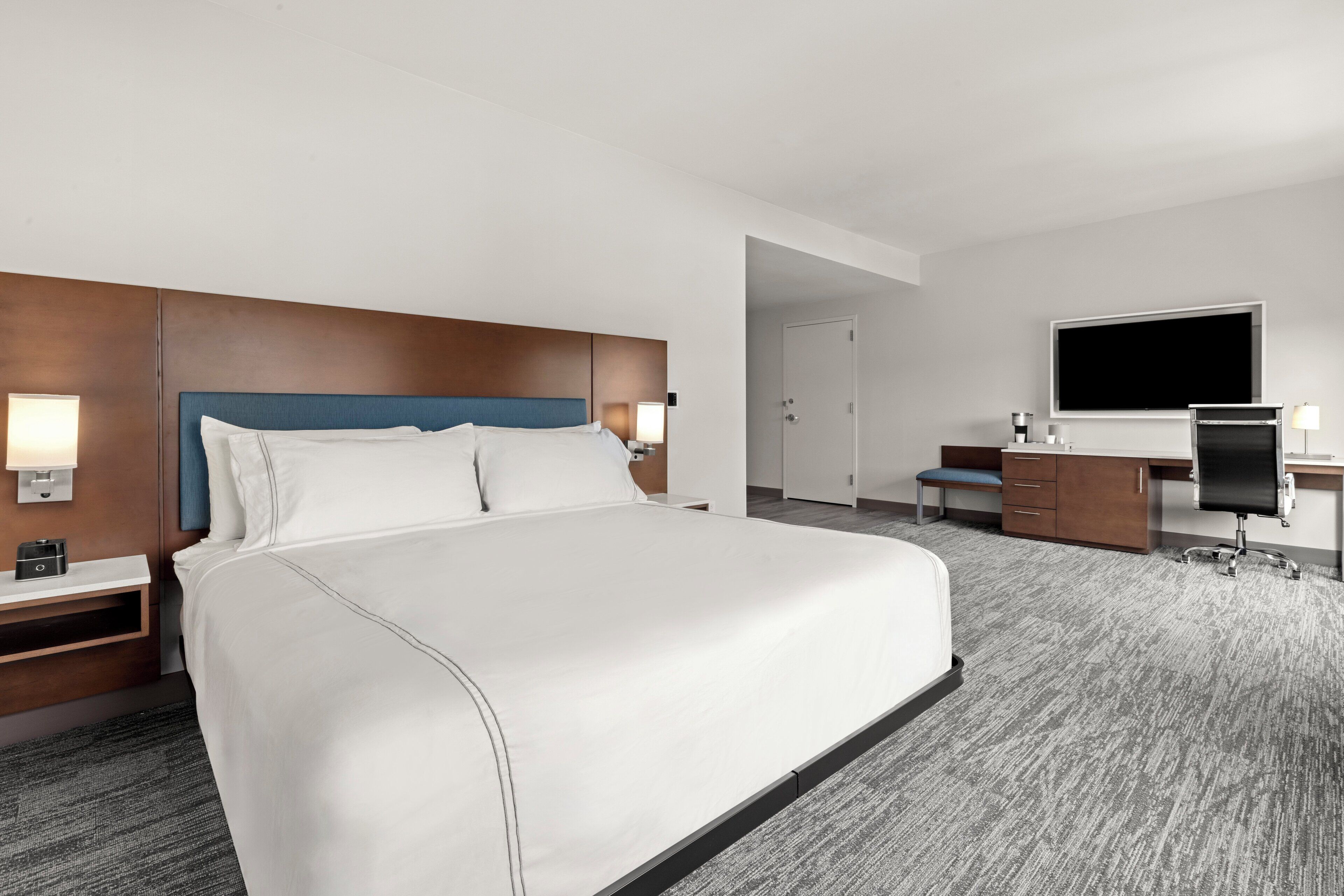 A hotel room with a large bed, a desk with a chair, a TV, and a wardrobe.