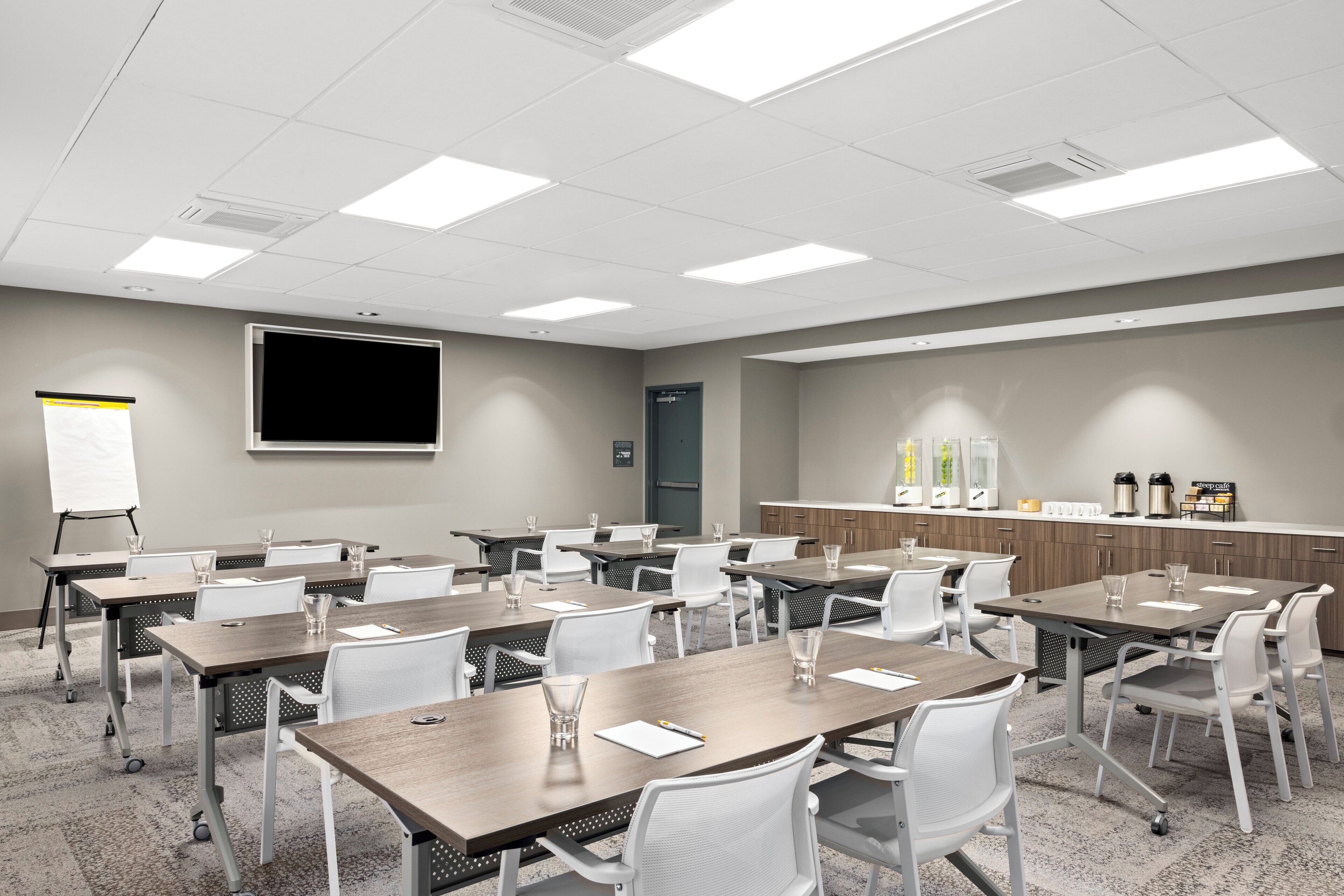 Une salle de conférence équipée de tables, de chaises, d’un tableau blanc et d’un coin cuisine.
