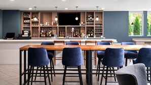 A modern bar area with a long wooden table, blue velvet chairs, and a well-stocked liquor shelf. - EVEN Hotel Portland – Beaverton by IHG (Portland)