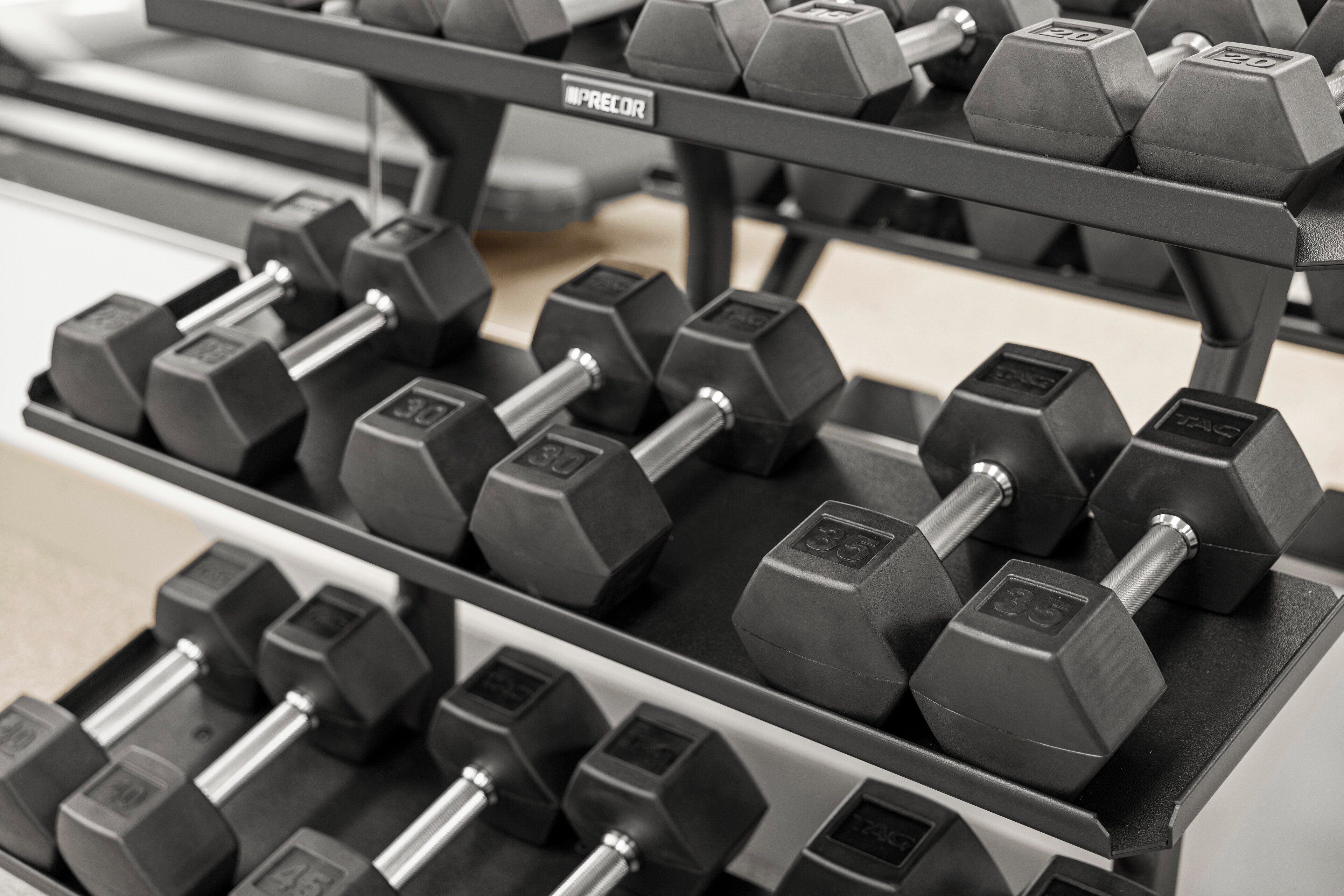 A rack of hexagonal dumbbells with weight markings, arranged on a shelf.