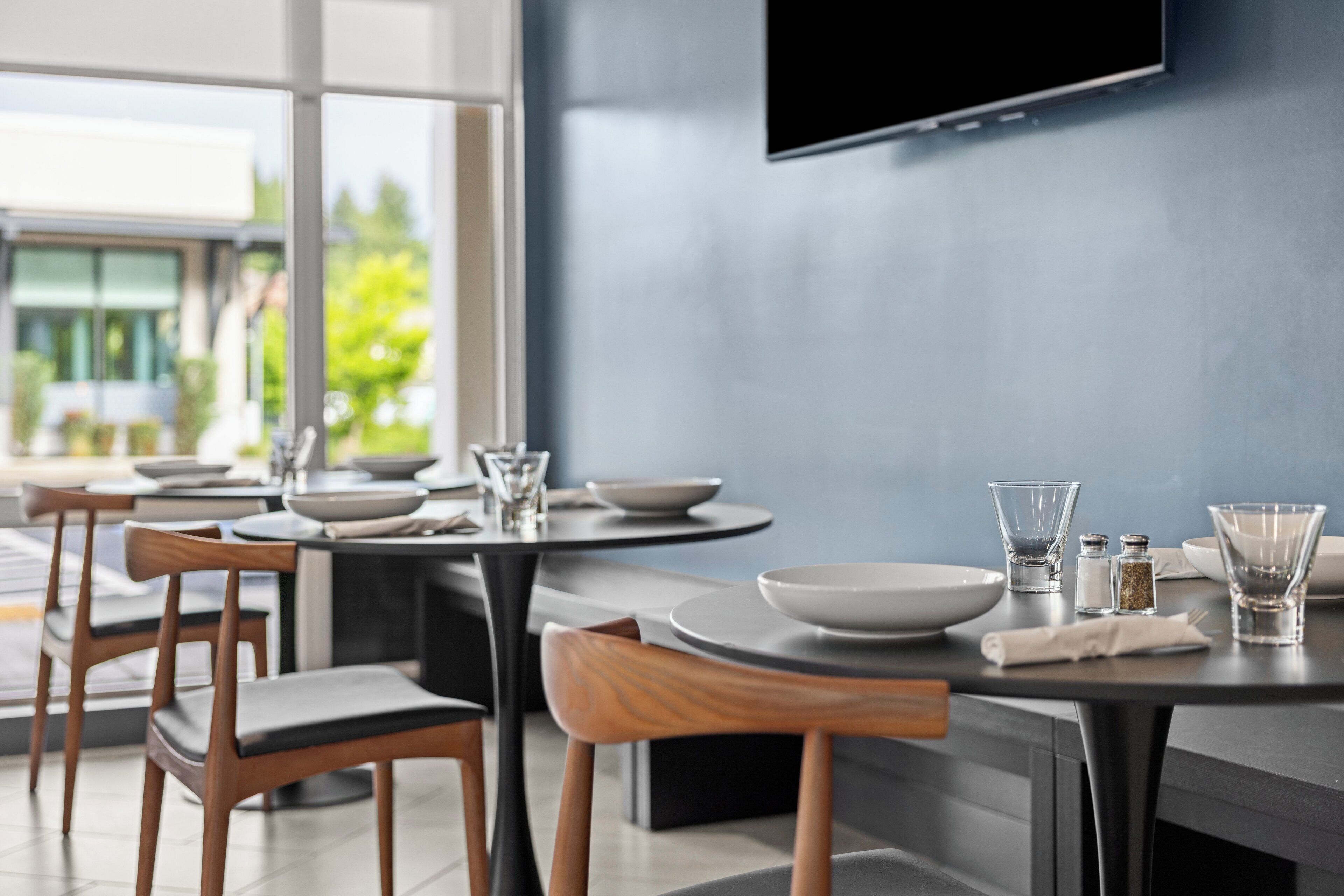 Un espace repas moderne avec des tables rondes, des chaises en bois et un téléviseur à écran plat fixé au mur.