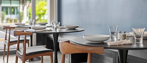 Un espace repas moderne avec des tables rondes, des chaises en bois et un téléviseur à écran plat fixé au mur.