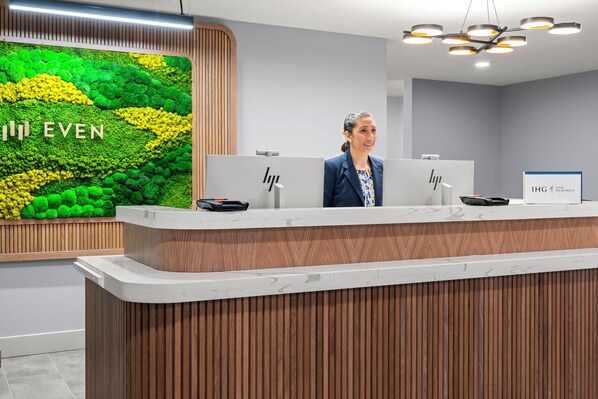 Un mostrador de recepción con detalles de madera, una pared verde con texto y un cartel de IHG Rewards.
