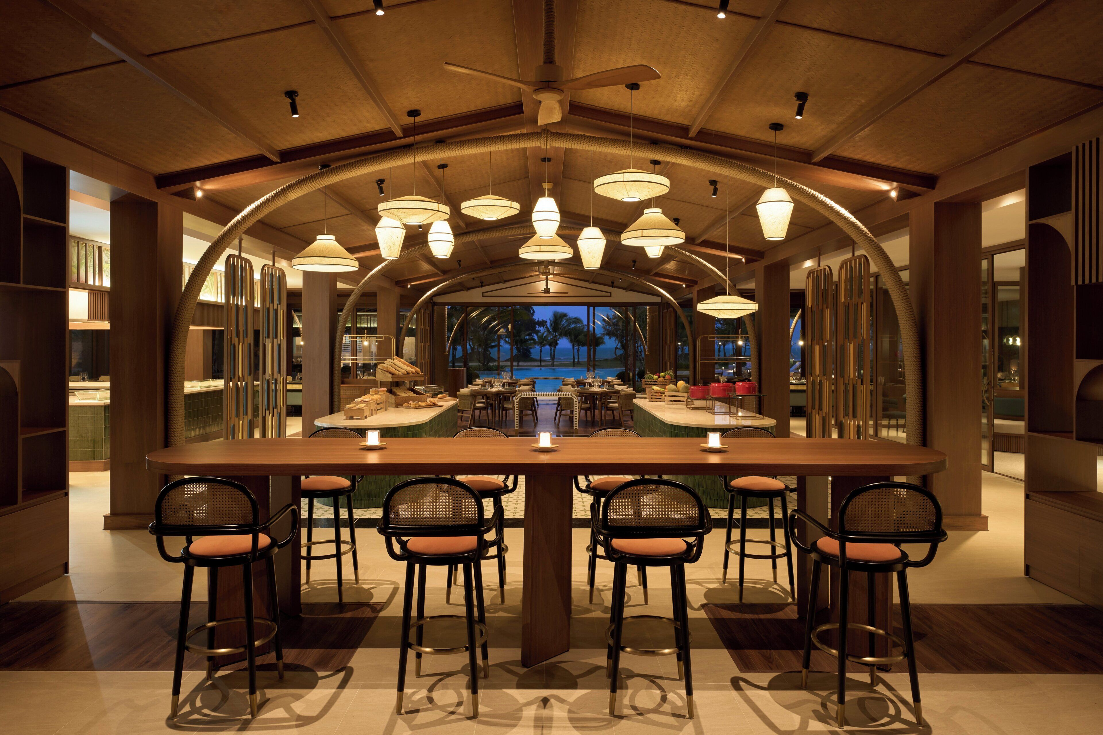 Un vaste espace dédié à la salle à manger, avec une longue table et de nombreuses chaises, un ventilateur de plafond et des luminaires suspendus.
