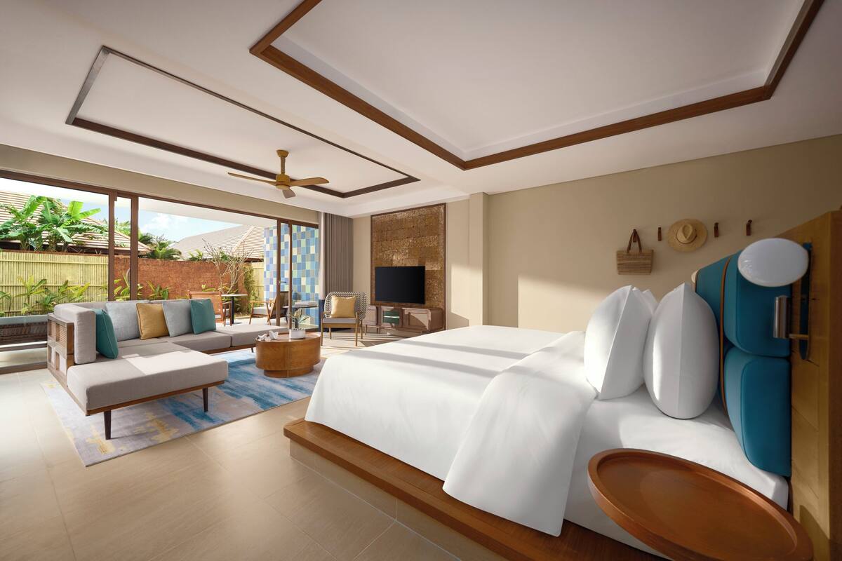Ein modernes Hotelzimmer mit einem großen Bett, einer Couch, einem Fernseher und einem Balkon mit Pflanzen.