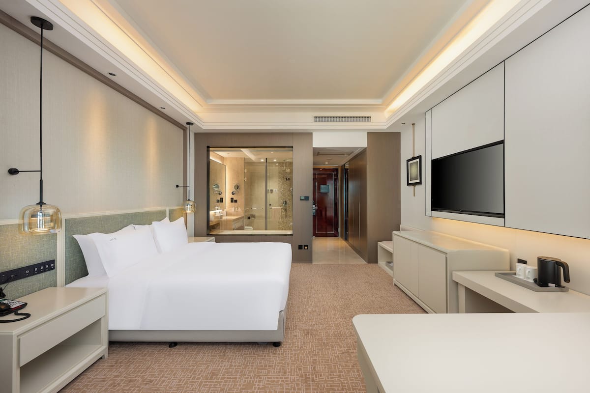 A hotel room with a large bed, bedside tables, a TV, and a bathroom visible through an open door.