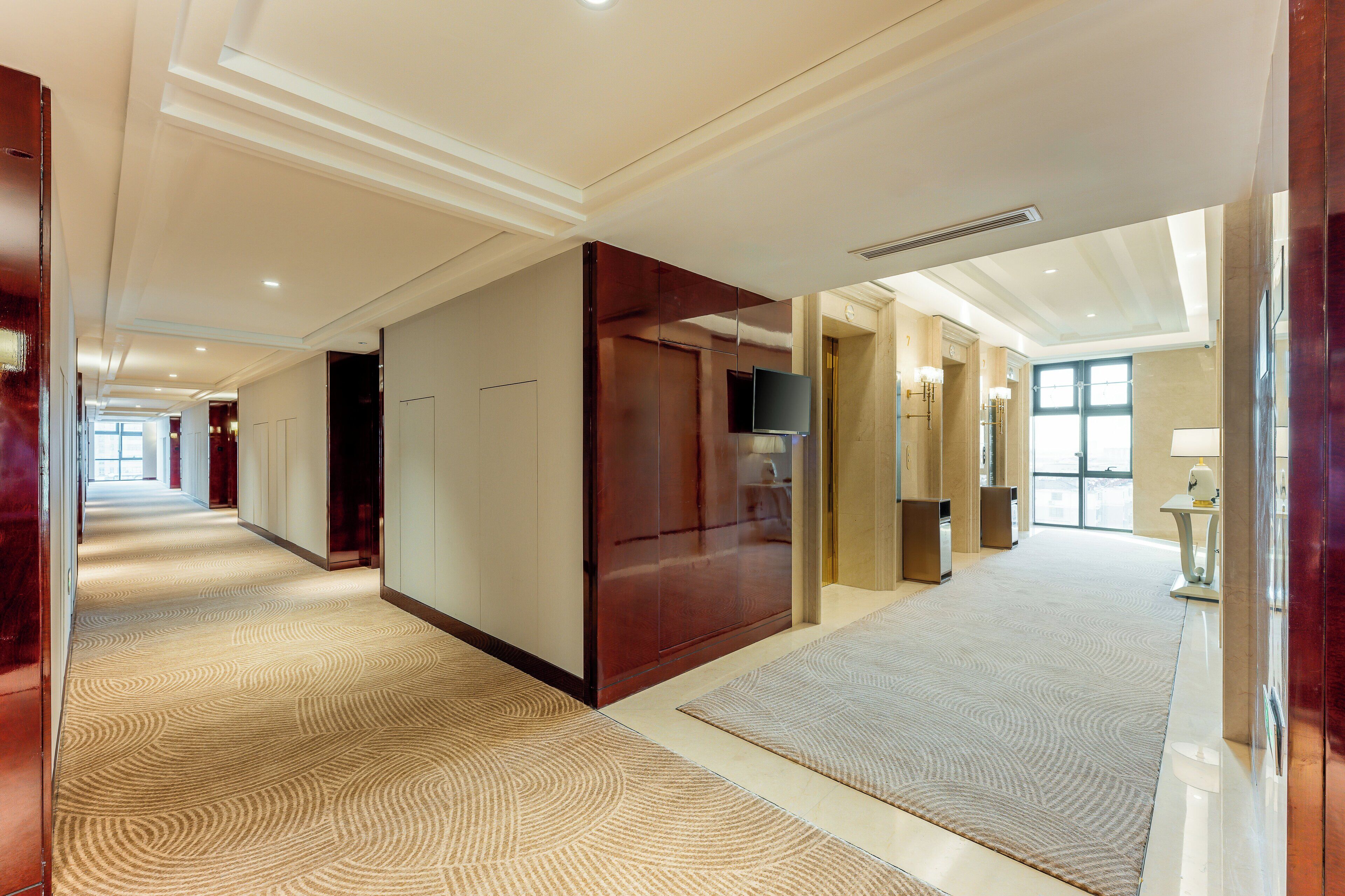 Un corridoio d'hotel con una moquette fantasia, rivestimenti in legno e un televisore fissato al muro.