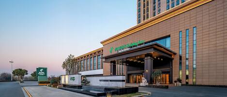 A modern hotel entrance with a large sign, a landscaped area with a water feature, and a parking lot.