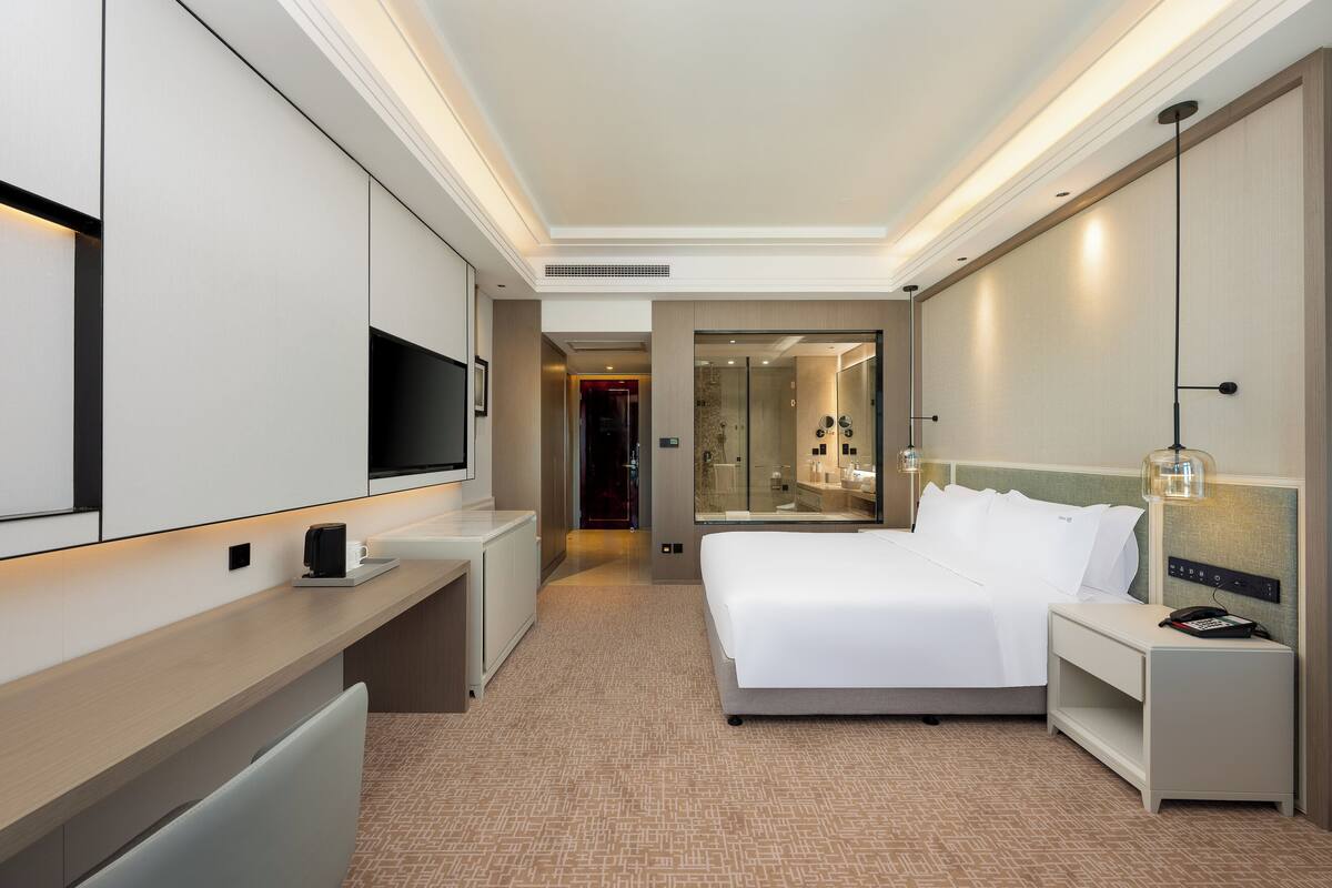 A hotel room with a bed, bedside table, TV, and a mirror.