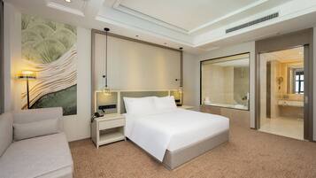 Una habitación de hotel moderna con una cama grande, un sofá, una mesita de noche con lámpara y un espejo amplio.
