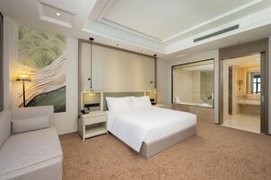 Una habitación de hotel moderna con una cama grande, un sofá, una mesita de noche con lámpara y un espejo amplio.