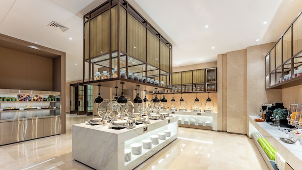 Un moderno vestíbulo de hotel con un mostrador de recepción de mármol, vitrinas de vidrio y una zona de buffet.