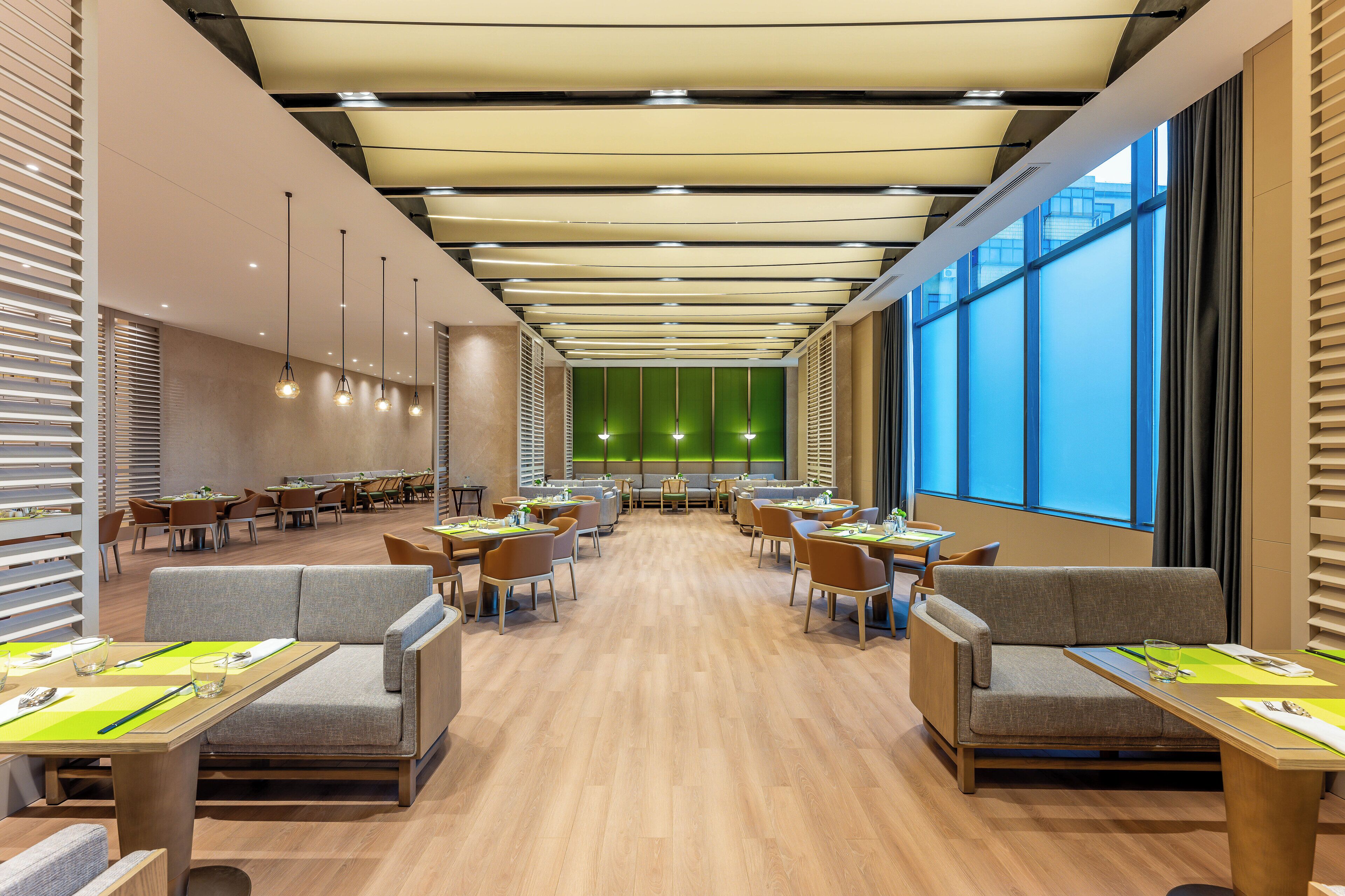 A modern dining area with tables and chairs, a green accent wall, and large windows.