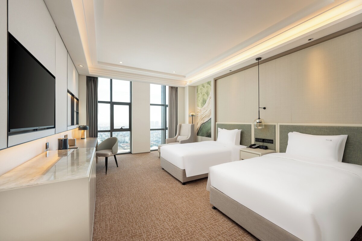 Une chambre d’hôtel avec deux lits, un bureau, une chaise, une télévision et une grande fenêtre.