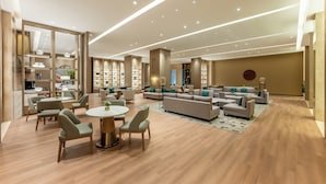 Un vestíbulo de hotel amplio y luminoso con un diseño moderno, que cuenta con una zona de estar central, una recepción y una gran estantería.