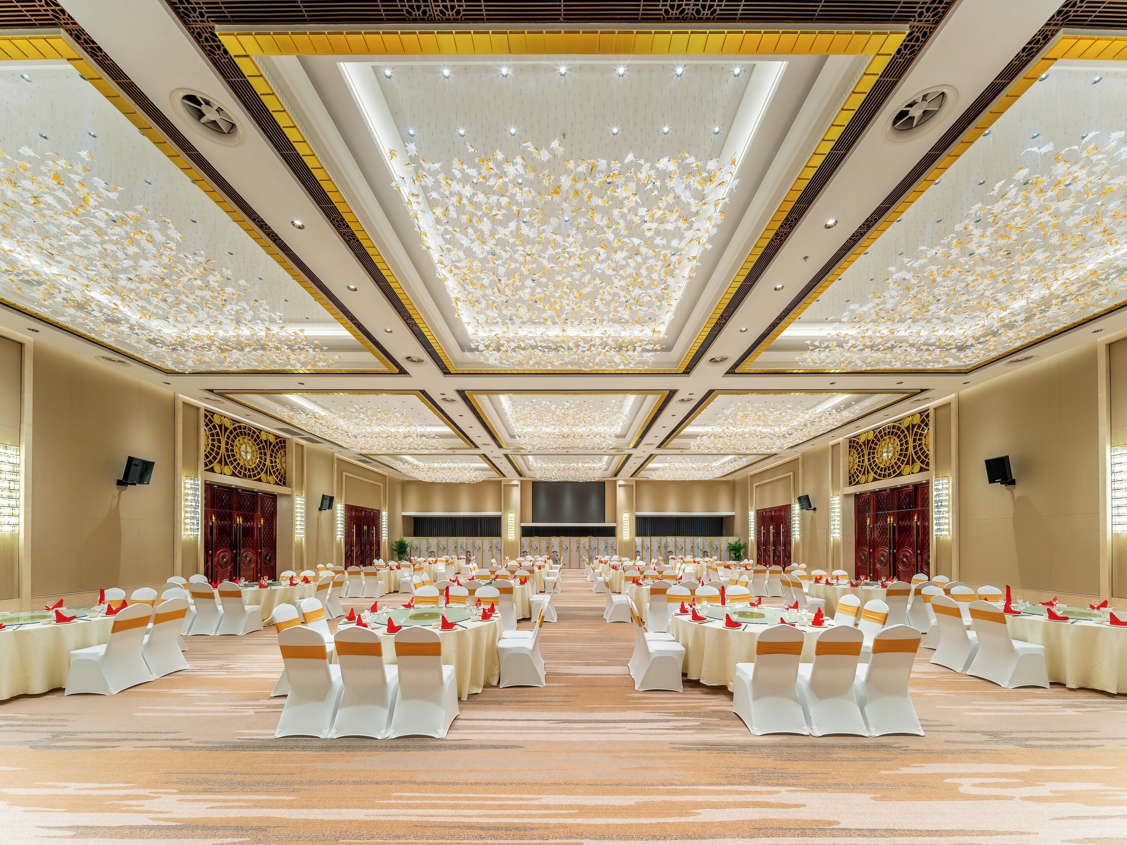 A banquet hall with rows of tables and chairs, a decorative ceiling, and a carpeted floor.