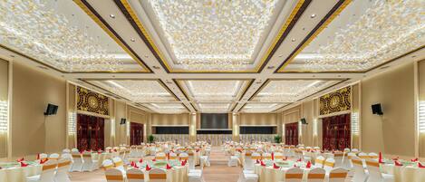 A banquet hall with rows of tables and chairs, a decorative ceiling, and a carpeted floor.