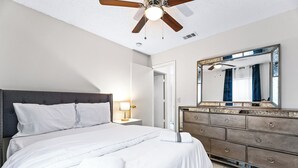 A neatly made bed with white linens, a wooden headboard, and a nightstand with a lamp. A large mirror with a decorative frame is above the dresser. - 4 bedrooms, 2 bathrooms 
 (Dallas)