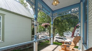 A covered porch with wooden chairs, a hanging flower basket, and a view of parked cars and a house in the background. - Main Street Gem-Steps to Downtown Telluride (Telluride)