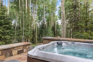 A hot tub in a forested area with stone walls and a stone ledge. - Be our Guest (House) (Telluride)