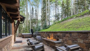 Une terrasse extérieure avec un sol en pierre, un foyer en pierre et plusieurs fauteuils de relaxation.