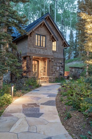 A stone house with a stone pathway leading to the entrance, surrounded by trees and greenery. - Be our Guest (House) (Telluride)
