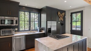 Une cuisine moderne avec des meubles de couleur sombre, des appareils électroménagers en acier inoxydable et un grand îlot central.