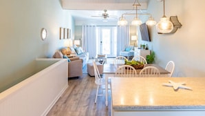 Un salon moderne avec un canapé, une table à manger et des chaises. On y trouve un ventilateur de plafond, des lampes suspendues et une fenêtre avec des rideaux.
