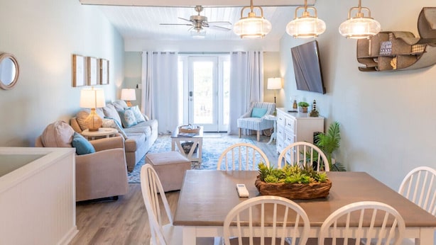 Un salon moderne avec un canapé, une table à manger et des chaises. Un téléviseur est fixé au mur et un ventilateur de plafond est installé.