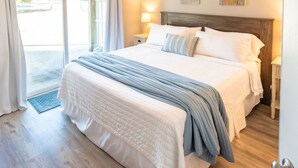Un lit bien fait, recouvert d’une couverture à rayures blanches et bleues, avec une tête de lit en bois et une table de chevet sur laquelle se trouve une lampe.