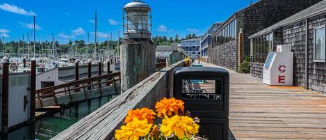A wooden pier with a row of buildings on one side and a marina on the other.