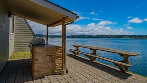 Un patio frente al lago con una parrilla de piedra y una mesa de picnic.