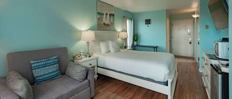 A bedroom with a bed, a sofa, a nightstand, a lamp, a television, and a microwave.