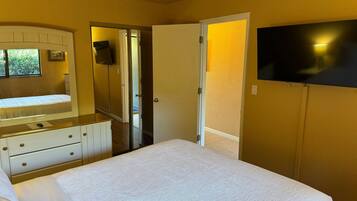 Une chambre à coucher comprenant un lit, une commode, un téléviseur fixé au mur et une porte donnant sur une autre pièce.