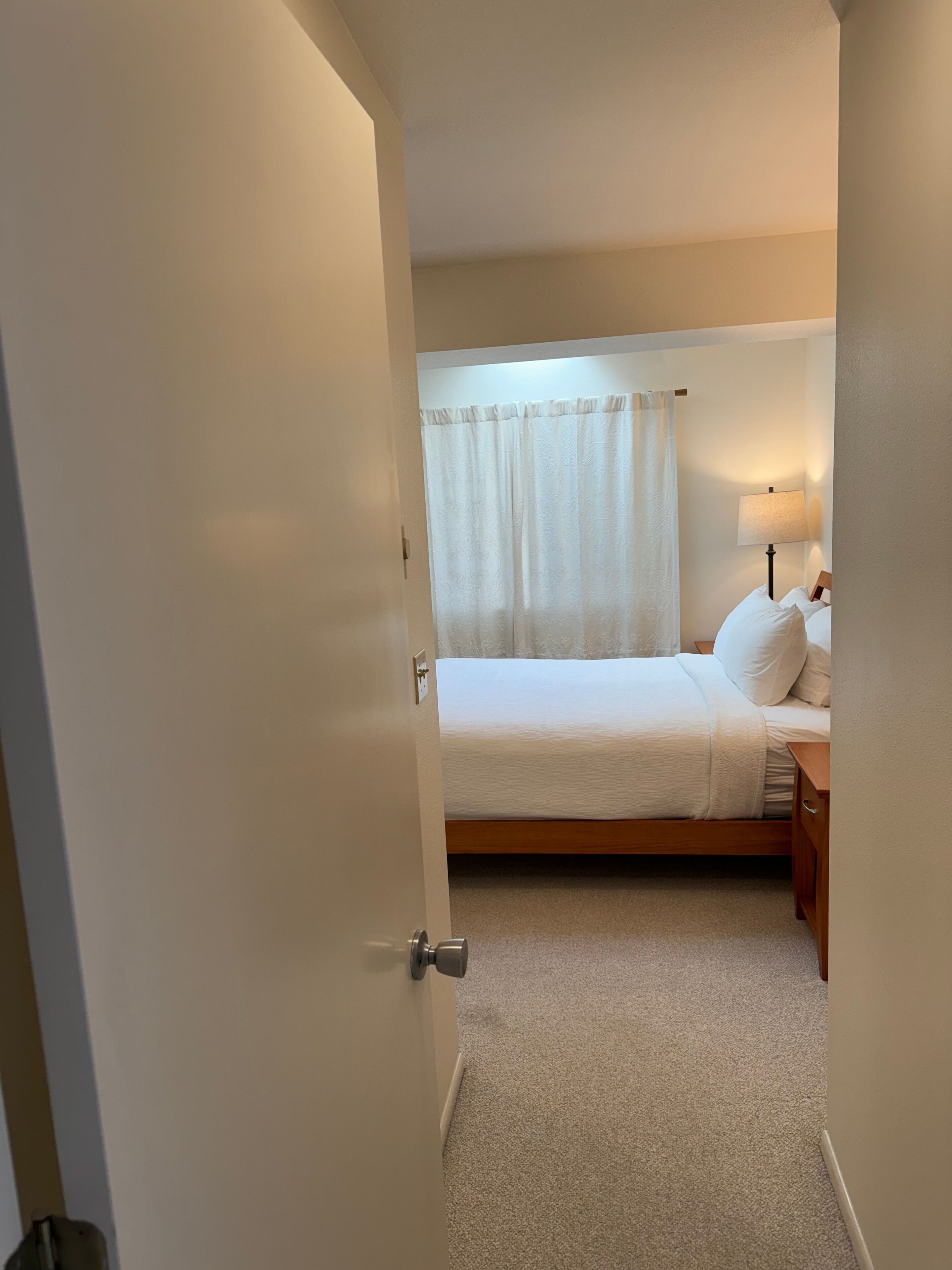 A bedroom with a bed, a nightstand, a lamp, and a window with curtains.