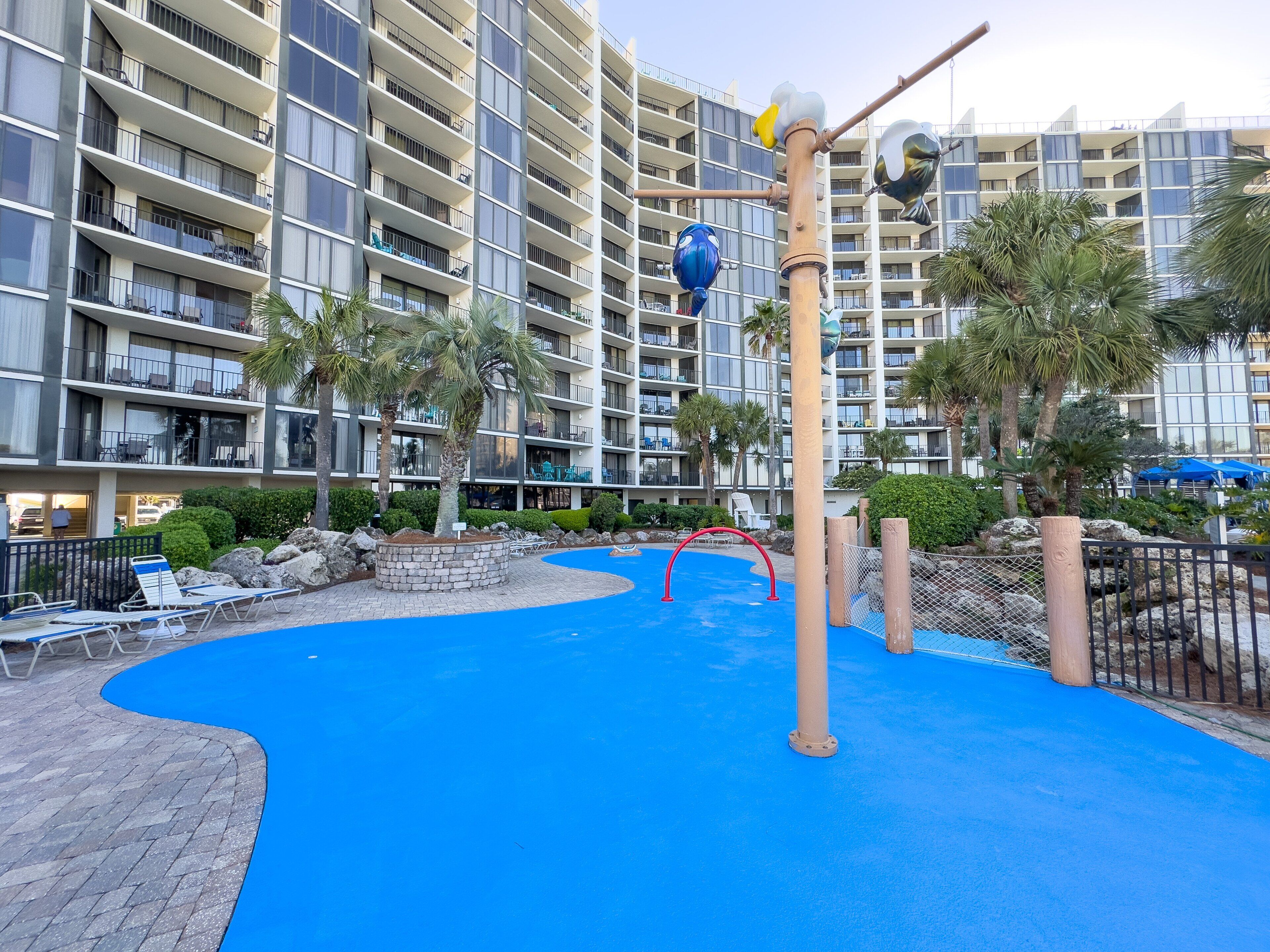 Un hôtel doté d’une piscine, de palmiers et d’un immeuble à plusieurs étages avec des balcons.